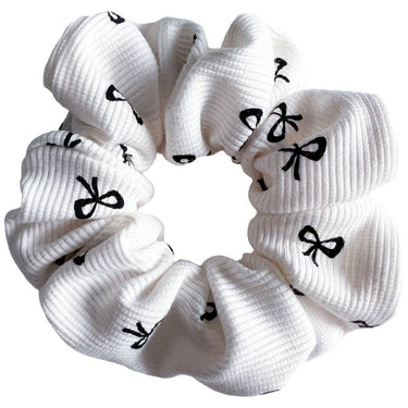 A white scrunchie with a ribbed texture, patterned with small black bow-tie shapes.